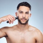 En person bruger en barbermaskine til at forme konturer og linjer i skægget.